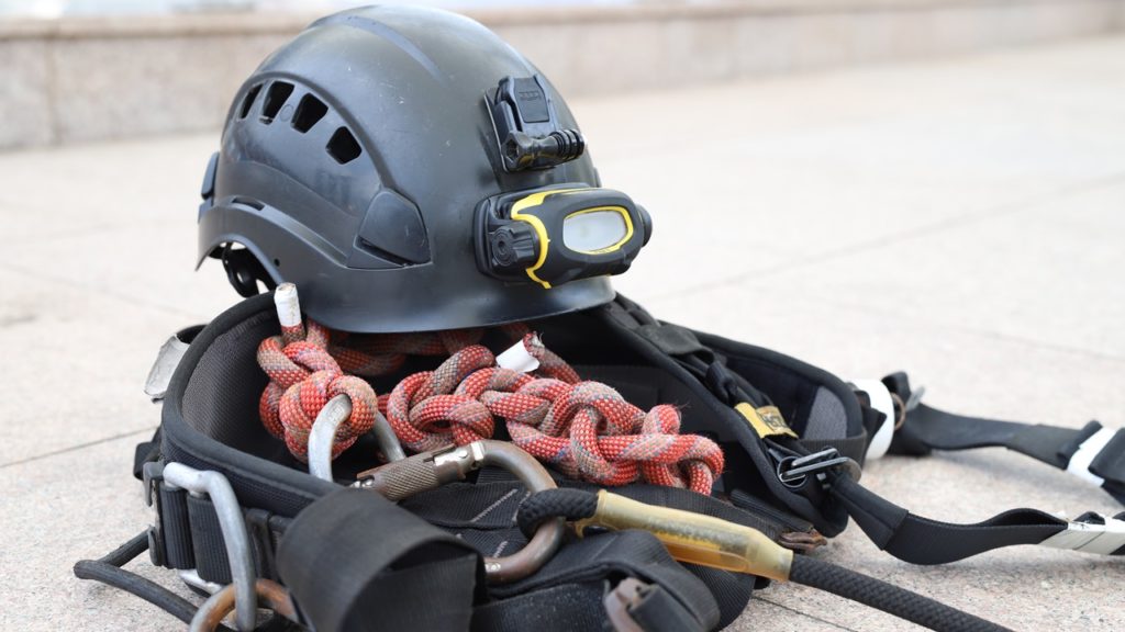A rigger's safety gear includes a harness, helmet, and safety shoes. 