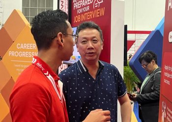 Two men talking in front of a poster.