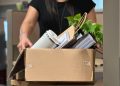 A woman carrying a box filled with office items.