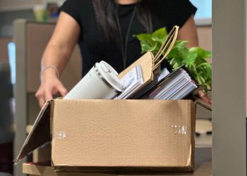 A woman carrying a box filled with office items.