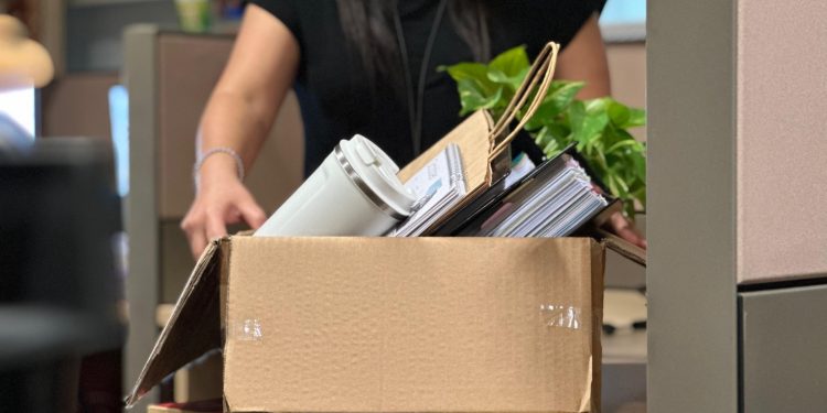 A woman carrying a box filled with office items.