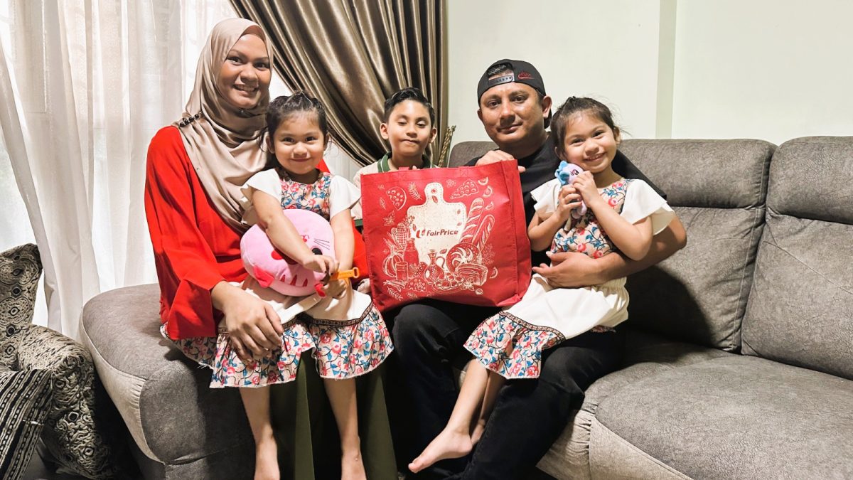 A family of five holding up a bag of groceries.
